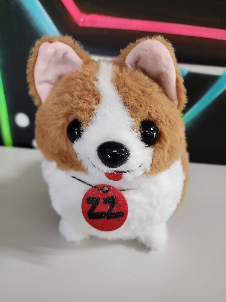 A plush corgi wearing a round red collar tag marked with a capital-letter zz, to identify the dog.
