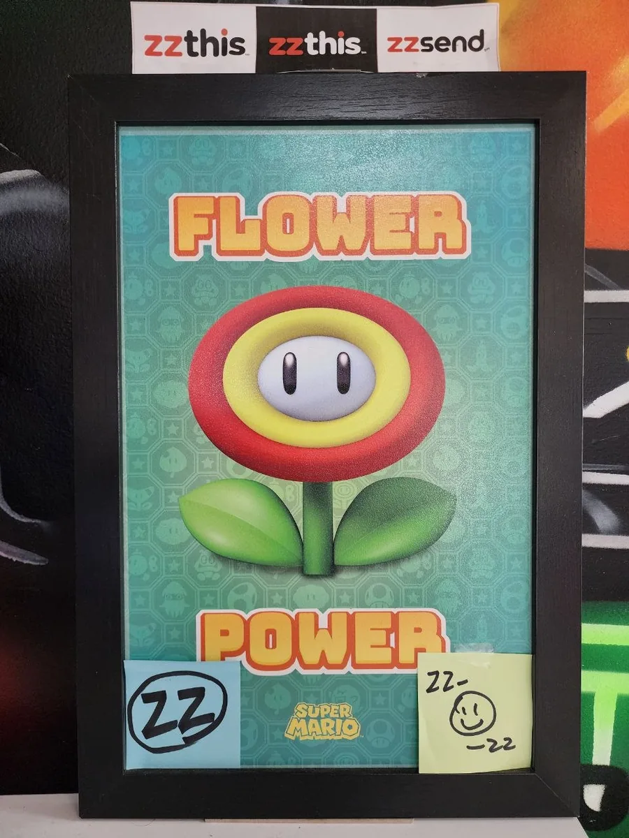 A framed Flower Power print with a circled capital-letter zz sticker in the lower left and a handwritten zz note with a smiley in the lower right.